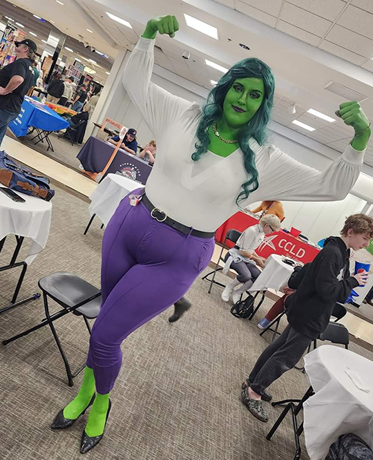 Woman dressed as she-hulk with green skin, hair, and purple pants