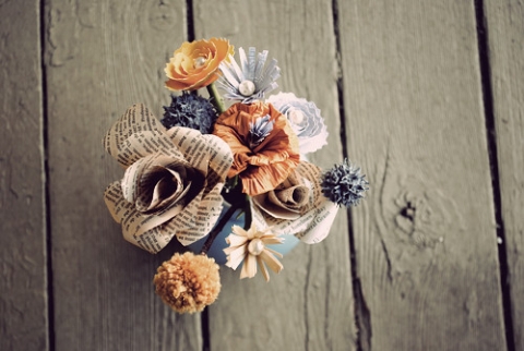 a bouquet of flower made out of old book pages and various other papers against a wood slatted background