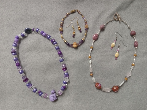Purple beaded nechlace with purple cat charm, purple and gold beaded earrings and bracelet, earrigns and neclace made from pink and silver beads with brown stones.