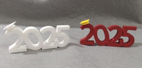 Two inch high statues saying 2025 in white with small graduation cap on the 2 and red 2025 with yellow cap on the 2..