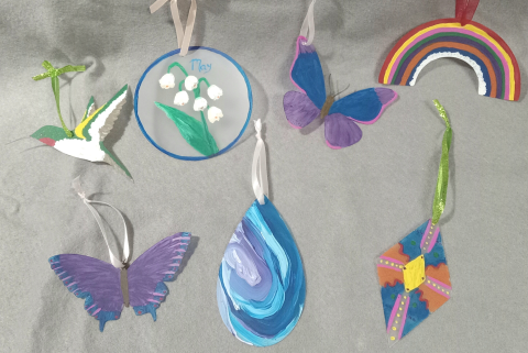 Seven suncatchers painted various colors in the shapes of a hummingbird, butterflies, rainbow, teardrop and diamond shapes.