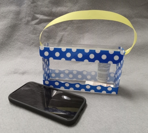 Clear plastic purse decorated with blue adn white polka-dot duct tape and yellow ribbon for handle. Phone shown for size of purse.