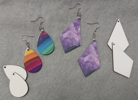 Four sets of earrings, two in teardrop shapes, one all white, one with rainbow pattern. Two sets of diamond shaped, one in white and one in purple amethyst.