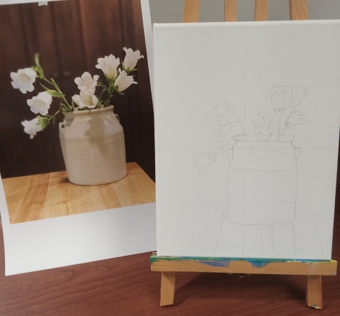 Photograph of flowers in a pot, canvas on an easel with drawing of flowers in a pot.