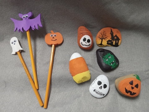 Three pencils topped with a ghost, a pumpkin adn a purple bat. Six rocks painted as a pumpkin, skull, Frankenstein, candy corn and haunted house.