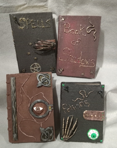 Four books, two black books, a red book and brown book decorated with spiders, spiders, snakes and skeleton hands.