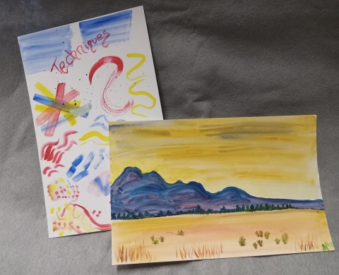 Paper with red, yellow and blue watercolor markings. Painting of a landscape with yellow and blue sky, purple mountains and tan field.