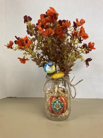 Mason jar filled with straw, artificial flowers in Fall colors, a miniature artificial bird, and a bailing twine bow.