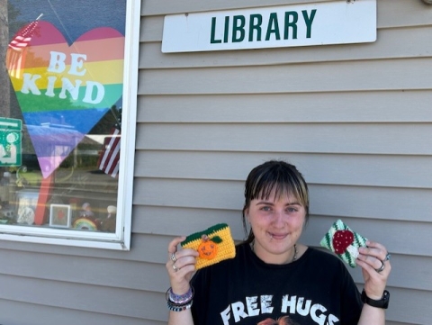Volunteer with crochet examples of mini wallets standing outside Van Etten library