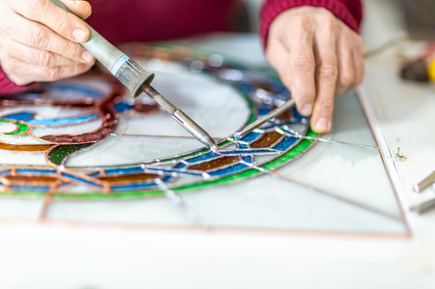Hands soldering pieces of colored glass together