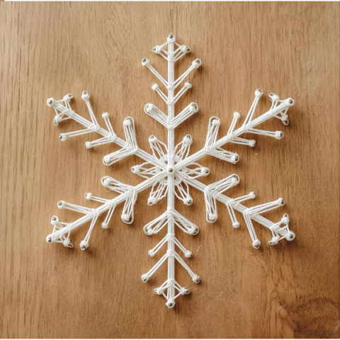 A white snowflake made with string art on a wooden board