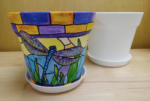 White pot and pot painted many colors with dragonfly in center.