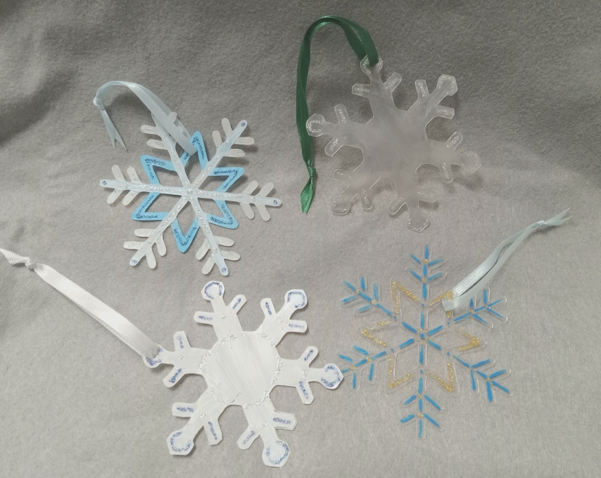 Four snowflakes painted silver, white, blue and gold with ribbons on each.